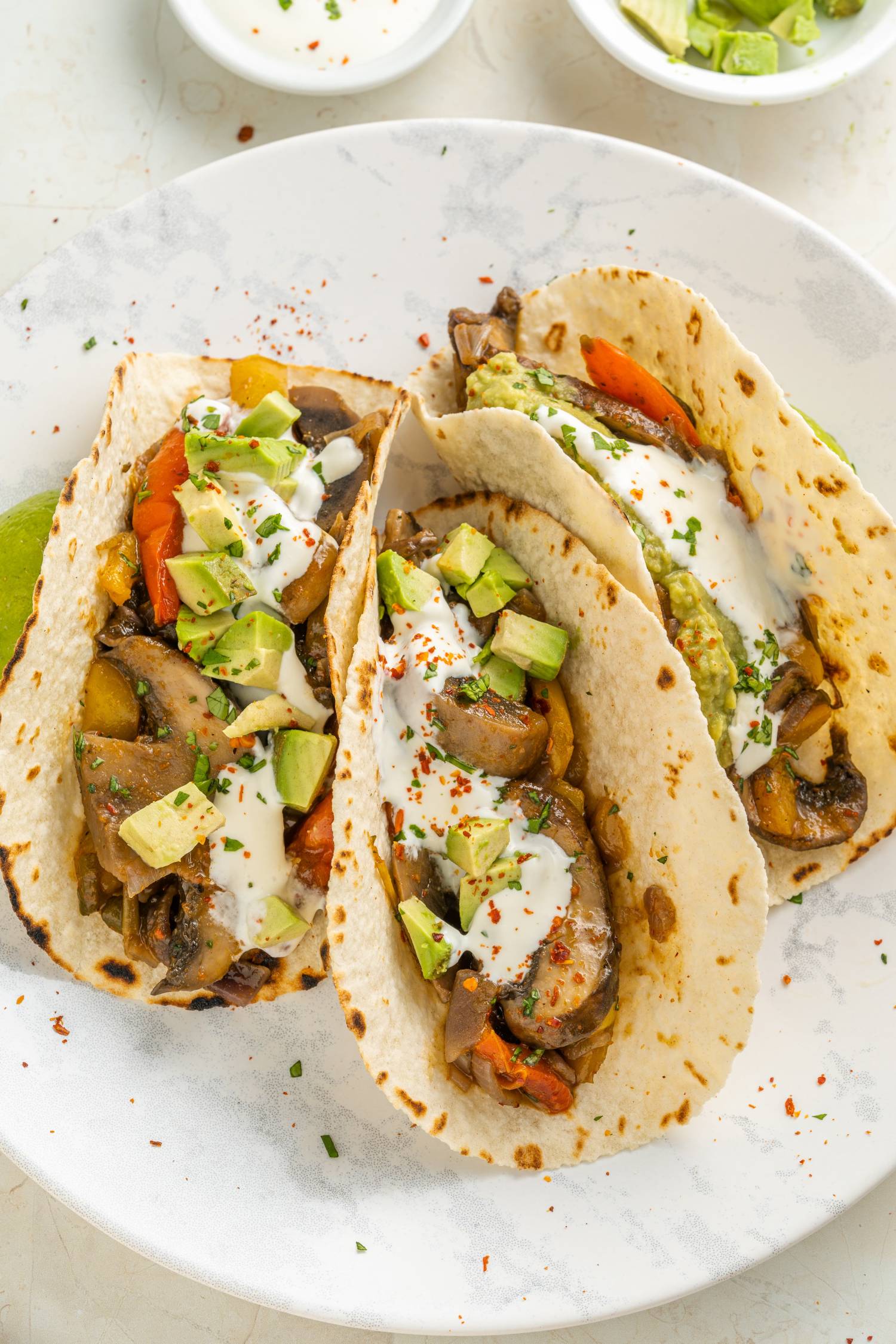 Vegan mushroom fajitas with portobellos, red onions, sliced peppers, avocado, and lime in three tortillas.