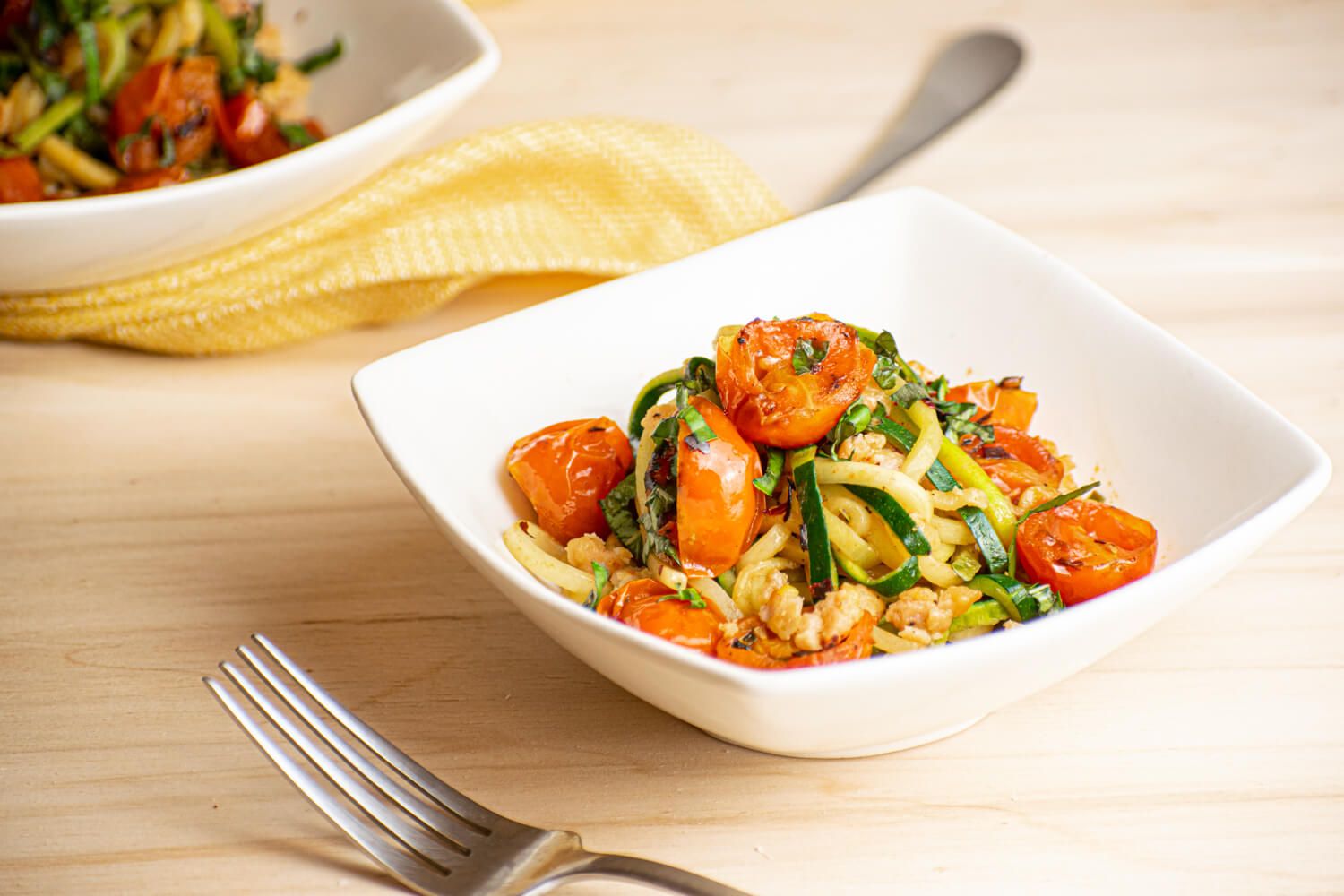 Garlic zucchini noodles with cherry tomatoes and ground sausage on a plate with Parmesan cheese.