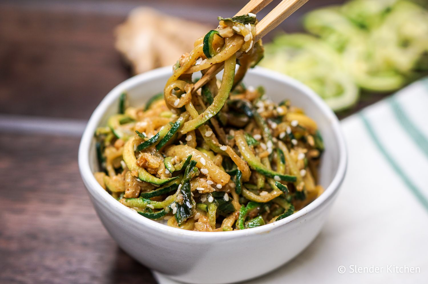 Zucchini noodles being picked up with a chopstick in a bowl.