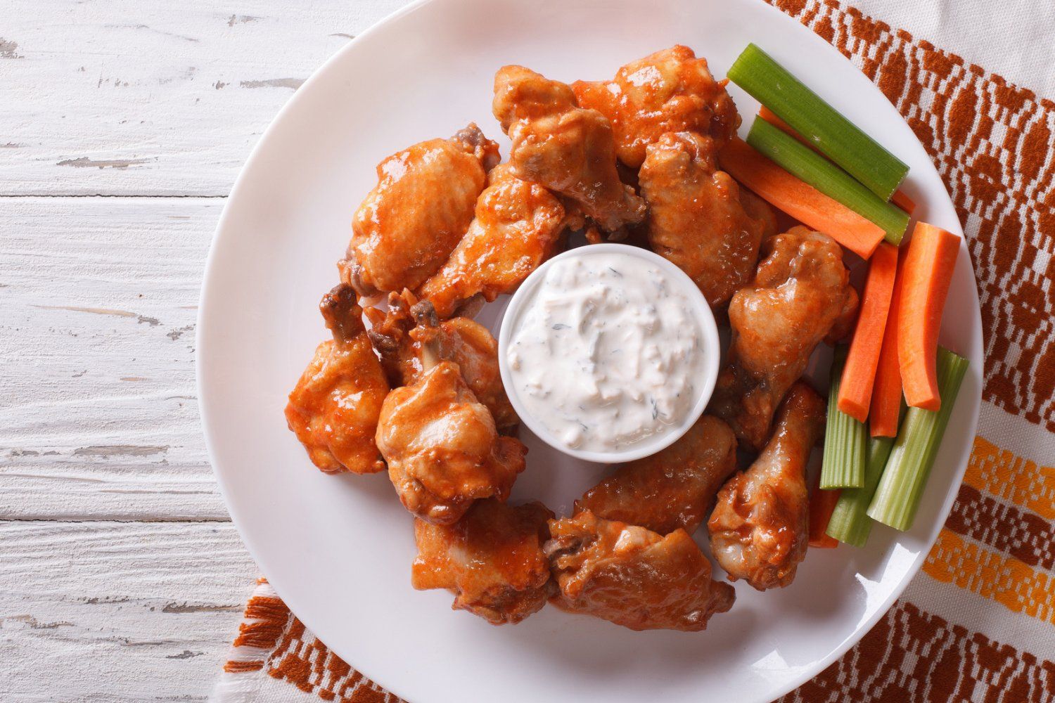 Baked buffalo wings on a plate with celery, carrots, and ranch dressing.