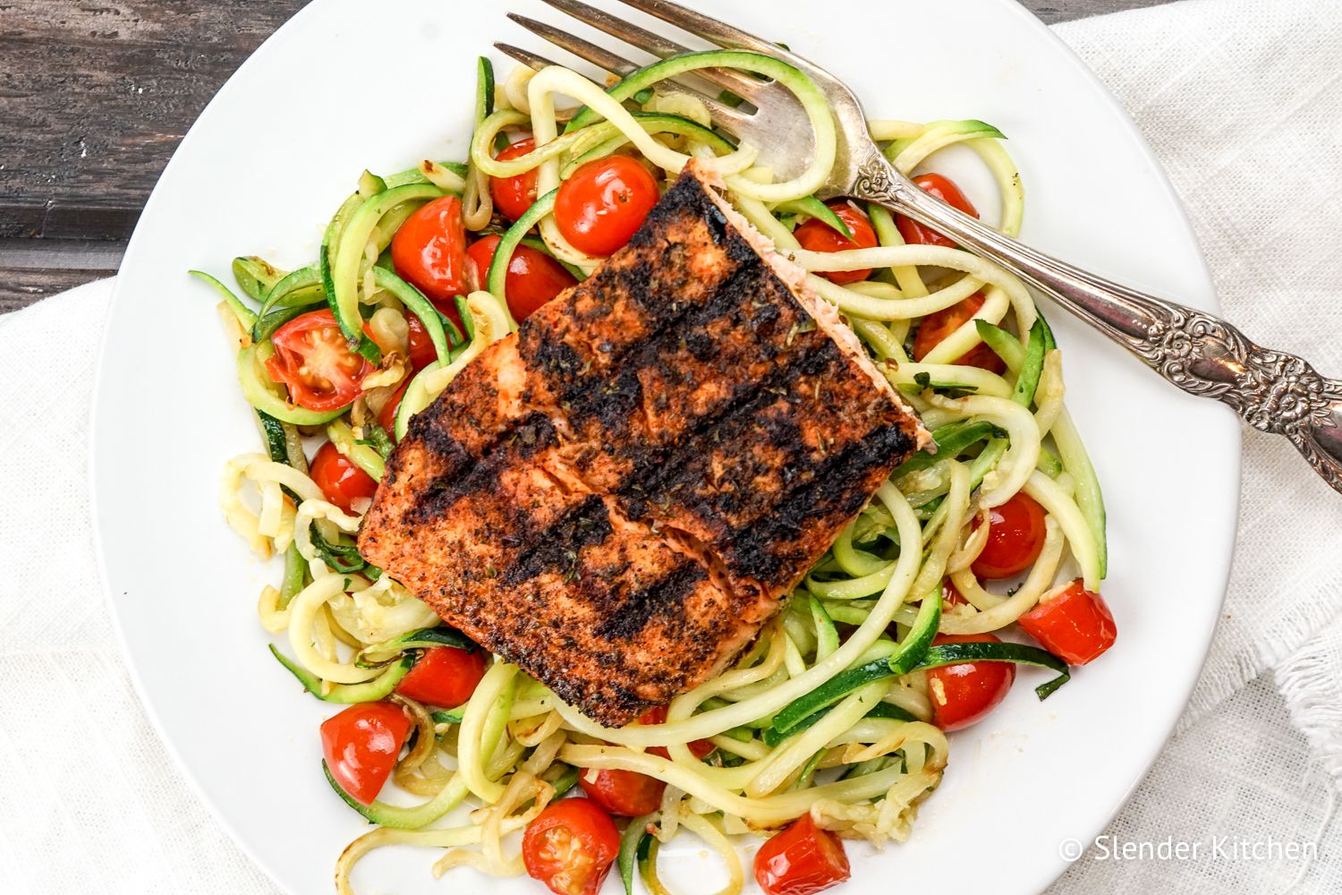 Zoodles on a white plate with salmon and tomatoes.