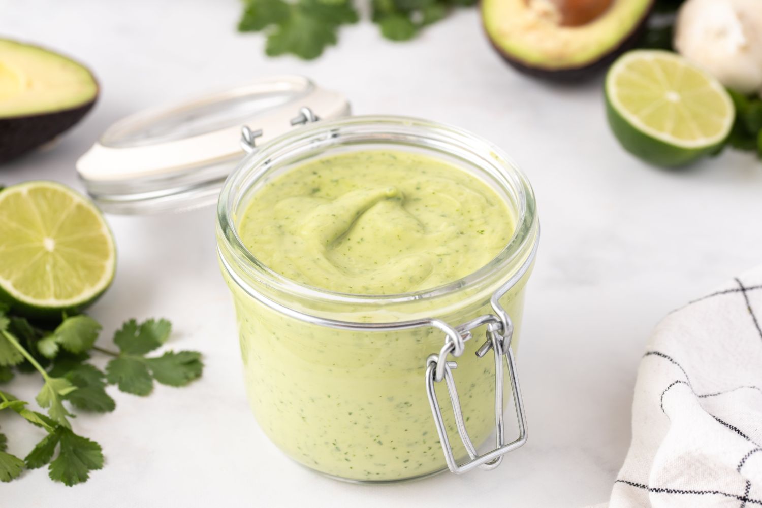 Creamy avocado dressing in a glass jar with avocado and lime on the side.