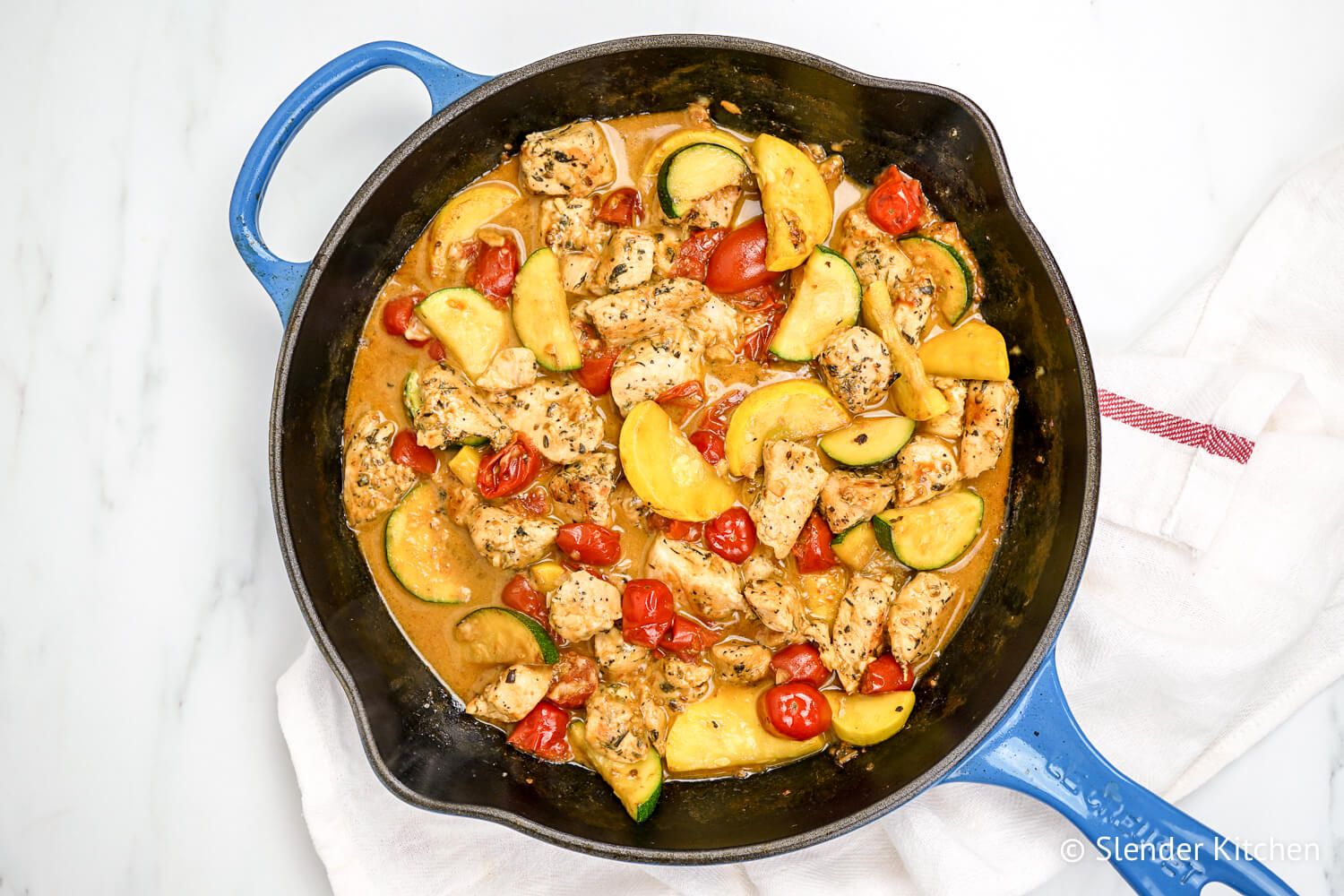 Creamy tuscan chicken with zucchini, summer squash, and tomatoes in a cast iron skillet.