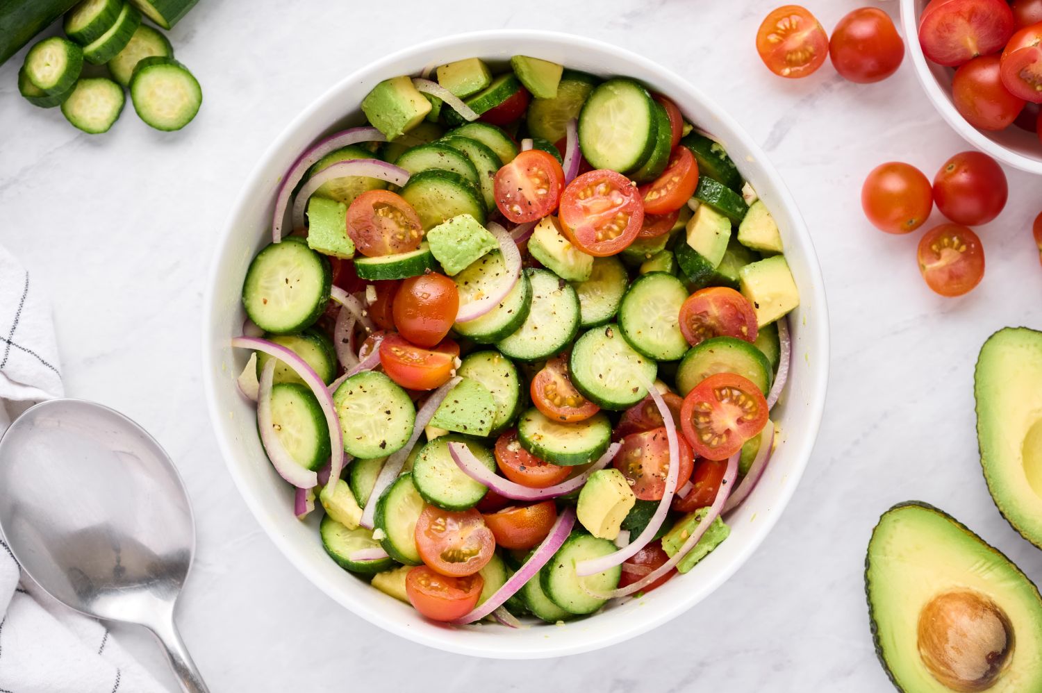 Cucumber and tomato salad with red onion in a white bowl with a wooden spoon.