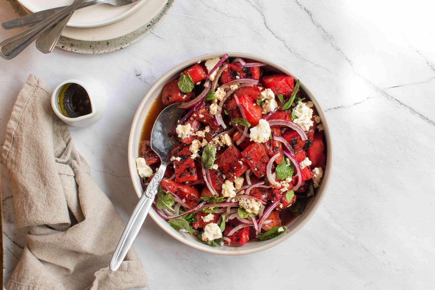 Grilled watermelon salad with cilantro, mint, red onion, and feta cheese in a white bowl.