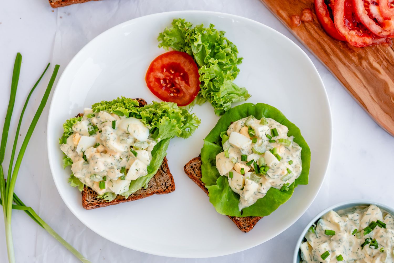 Herby egg salad with hard boiled eggs, yogurt, and fresh herbs served on whole wheat bread with lettuce and tomatoes.