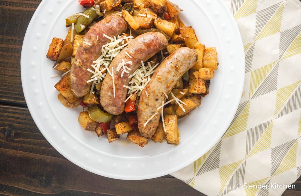 Roasted chicken sausages, potatoes, peppers, and onions on a plate with salt and pepper.