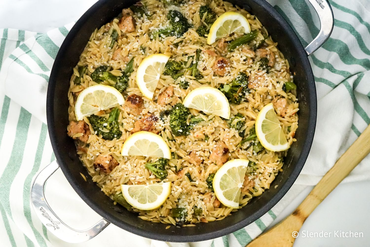 Lemon orzo and broccoli with chicken sausage in a skillet with a blue and white napkin.