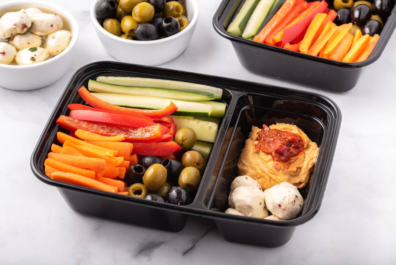 Mediterranean bistro box with olives, hummus, mozzarella, and sliced vegetables.