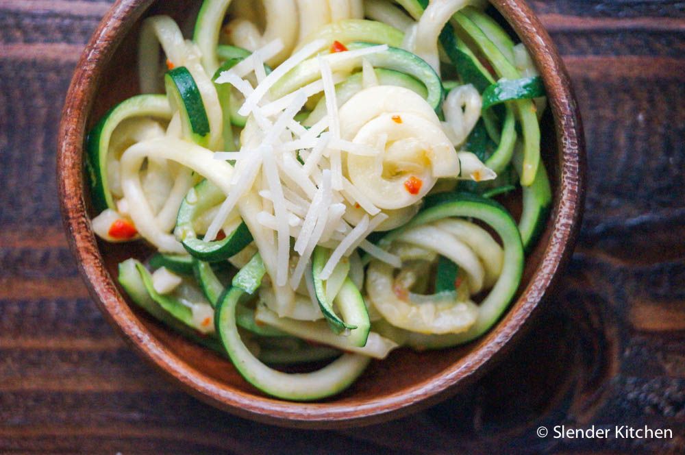 Zucchini noodles in a wooden bowl with Parmesan cheese and red pepper flakes.