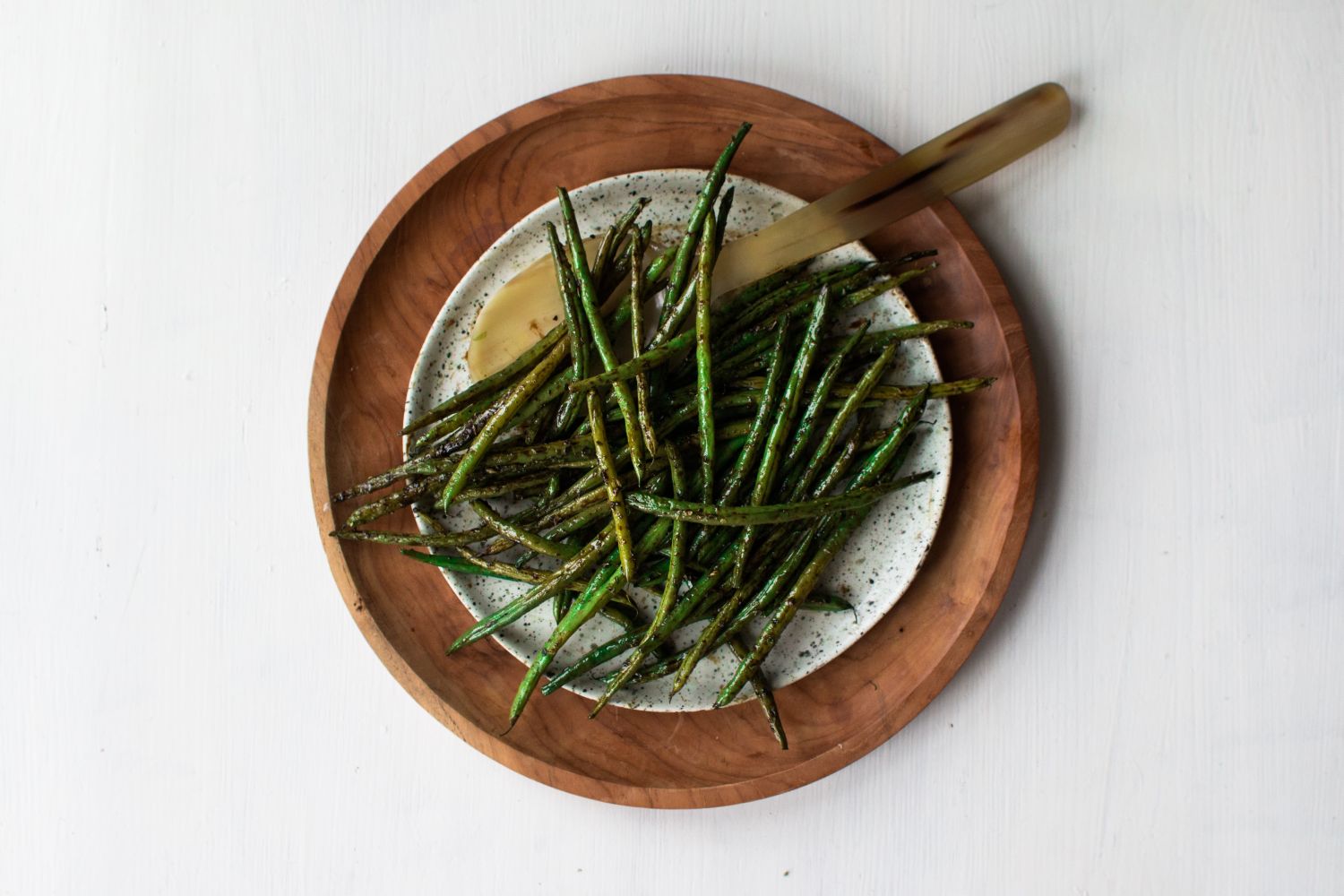 Roasted green beans on a plate with garlic, olive oil, salt, pepper, and a small fork.