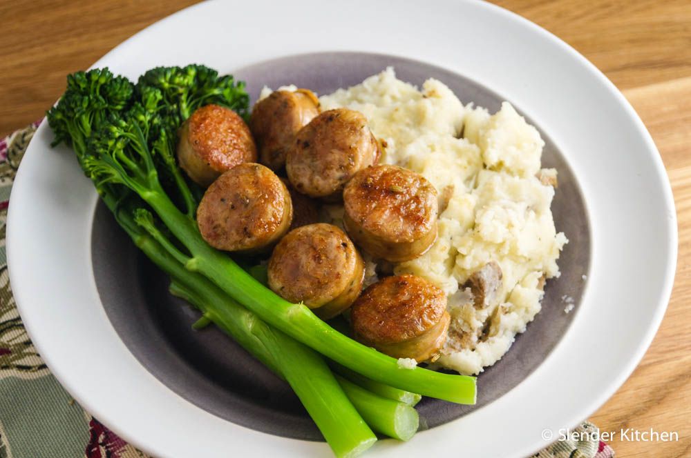 Sausage, mashed potatoes, and broccolini on a plate with a napkin and fork.