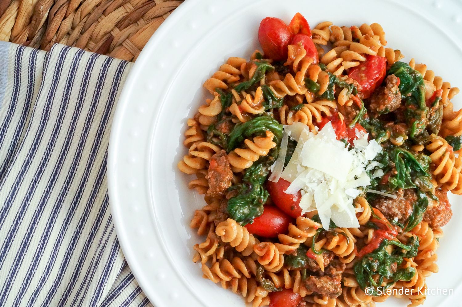 Sausage, tomato, and spinach Arrabiata pasta in a white dish topped with parmesan cheese.