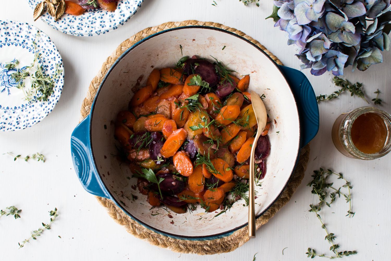 Roasted carrots with honey, garlic, and fresh parsley in a dish with fresh herbs on the side.