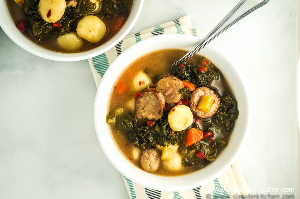 Sausage and gnocchi soup with spinach and tomatoes in a bowl with a spoon.