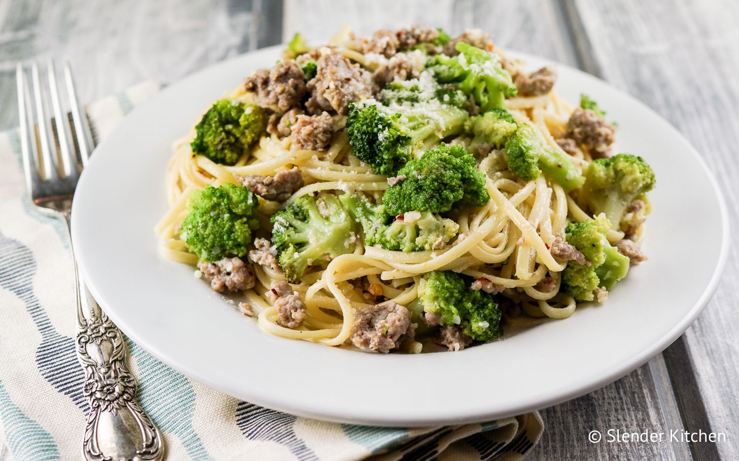 Turkey sausage and broccoli pasta on a plate with a fork and blue napkin.