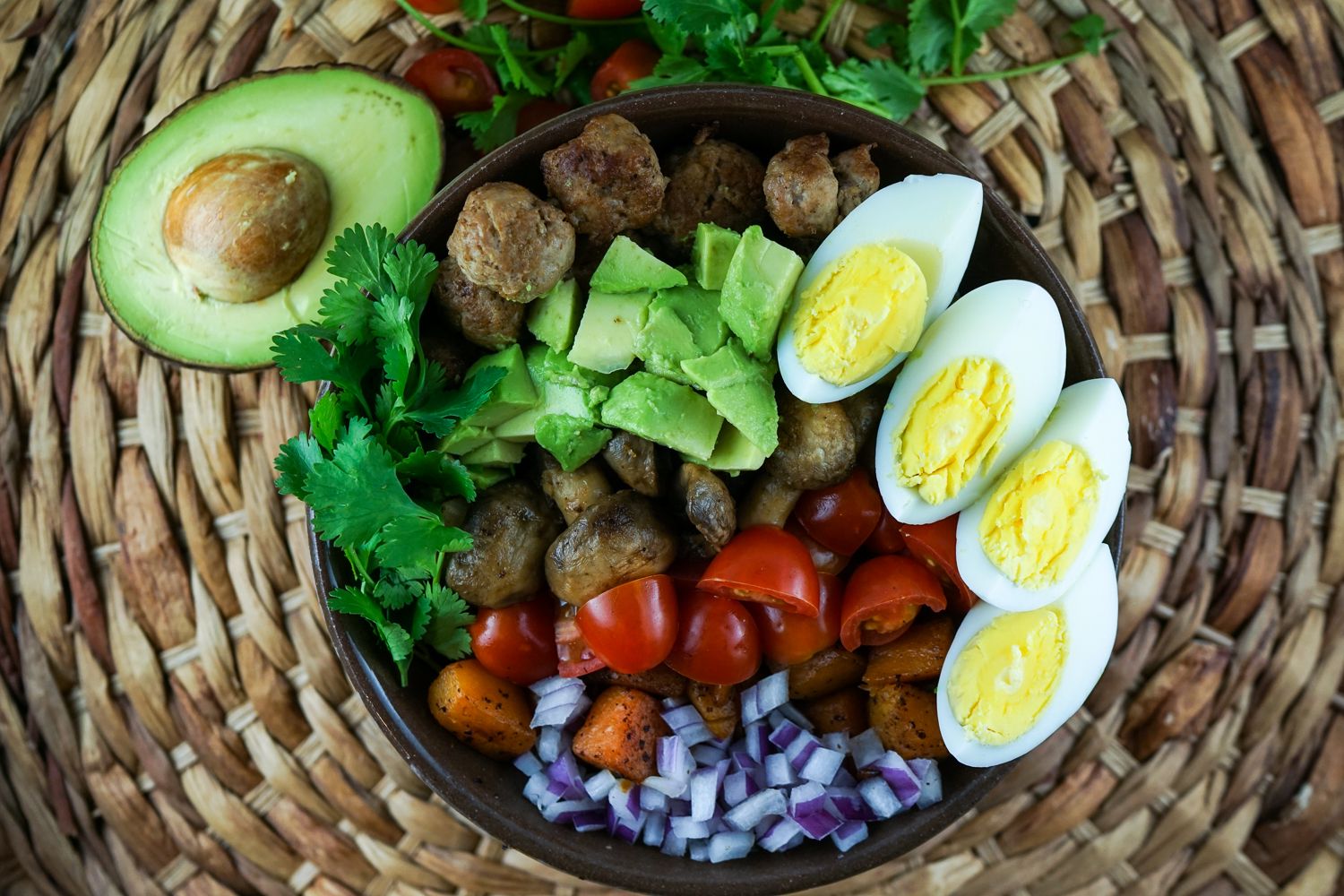 Breakfast salad with avocado, boiled eggs, butternut squash, sausage, red onion, and avocado in a wooden bowl.