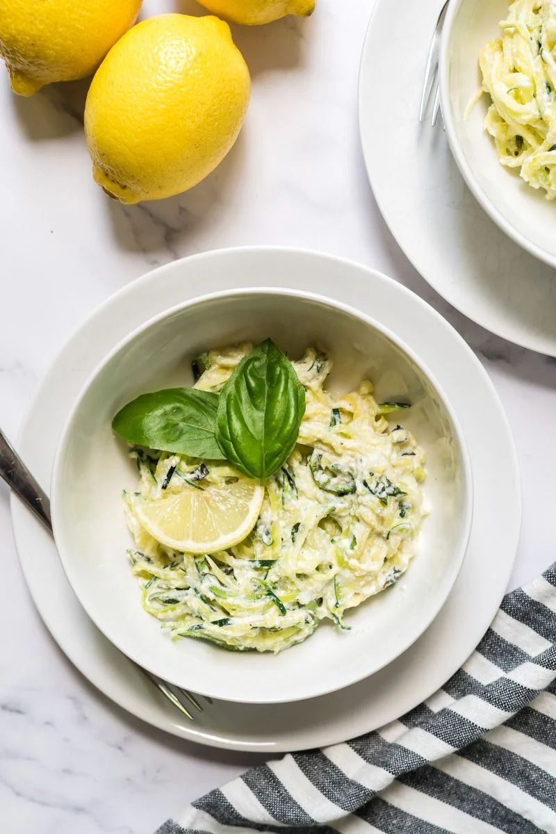 Creamy zucchini noodles with ricotta cheese and lemon in a white bowl with fresh basil.