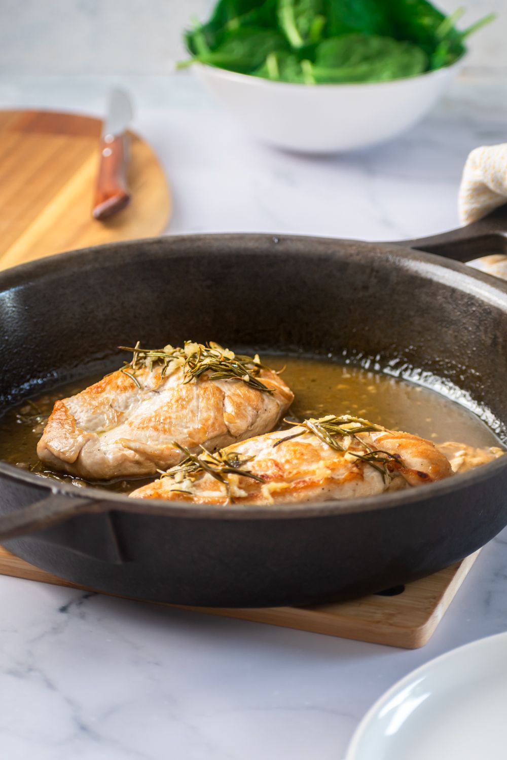 Chicken breast with rosemary in a garlic, lemon, and butter pan sauce in a skillet.