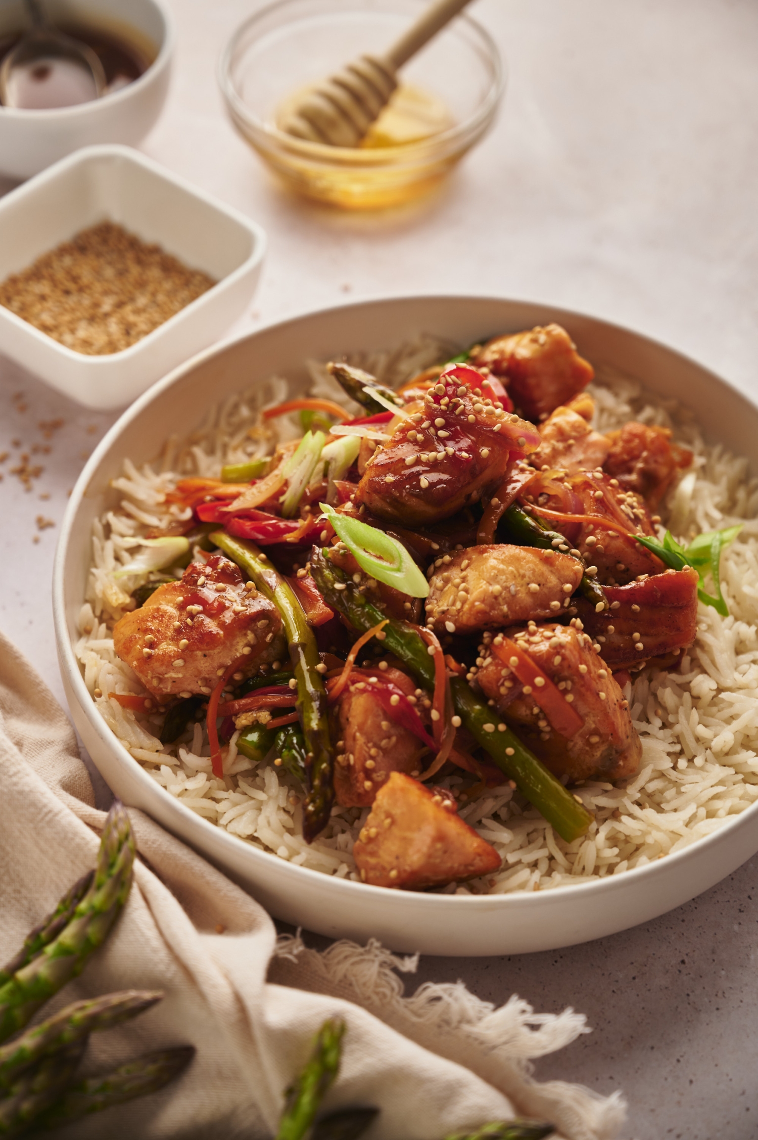 Salmon and vegetable stir fry with salmon chunks, asparagus, carrots, and red peppers served in a bowl with rice. 