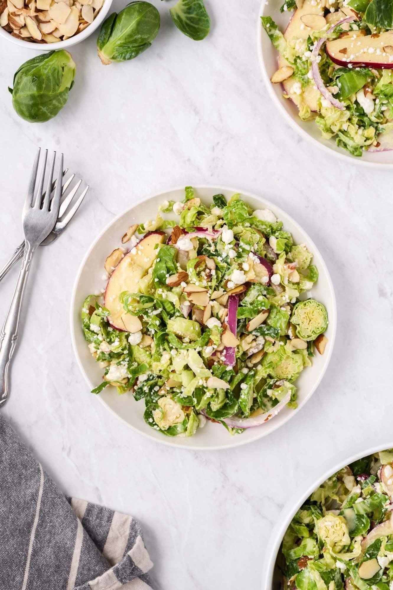 Honey dijon shaved brussels sprouts salad with sliced apples, almonds, goat cheese, and red onions.