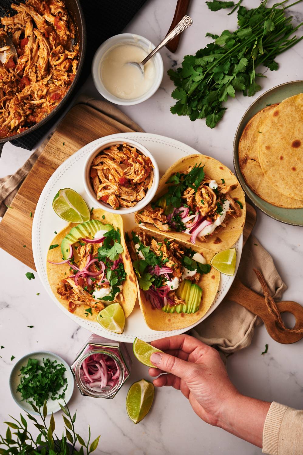 Tacos with shredded chicken in tomato salsa with cilantro, limes, sour cream, and onions.