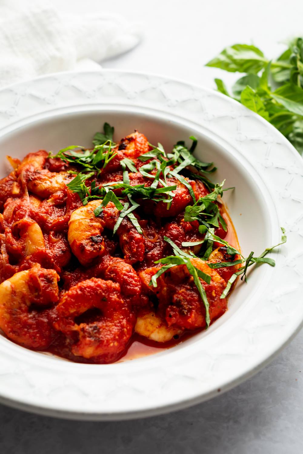 Spicy shrimp fra diavolo in a white bowl with tomato sauce, basil, and shrimp.