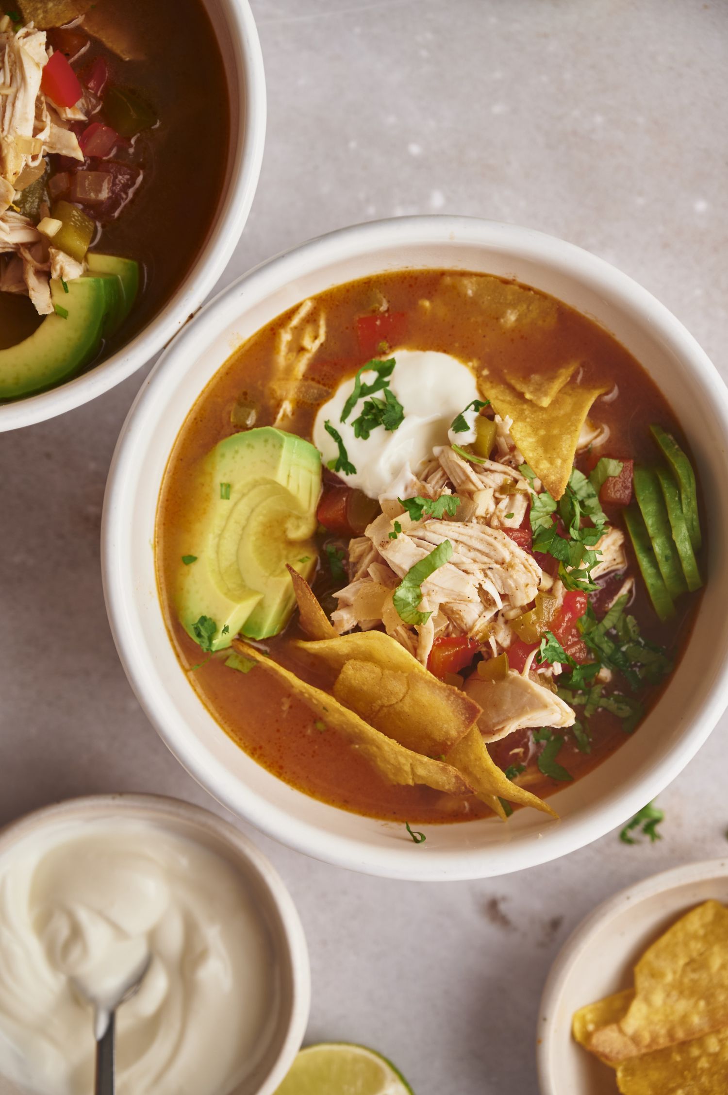 Chicken fajita soup with avocado, sour cream, tortilla chips, and cilantro in a white bowl.