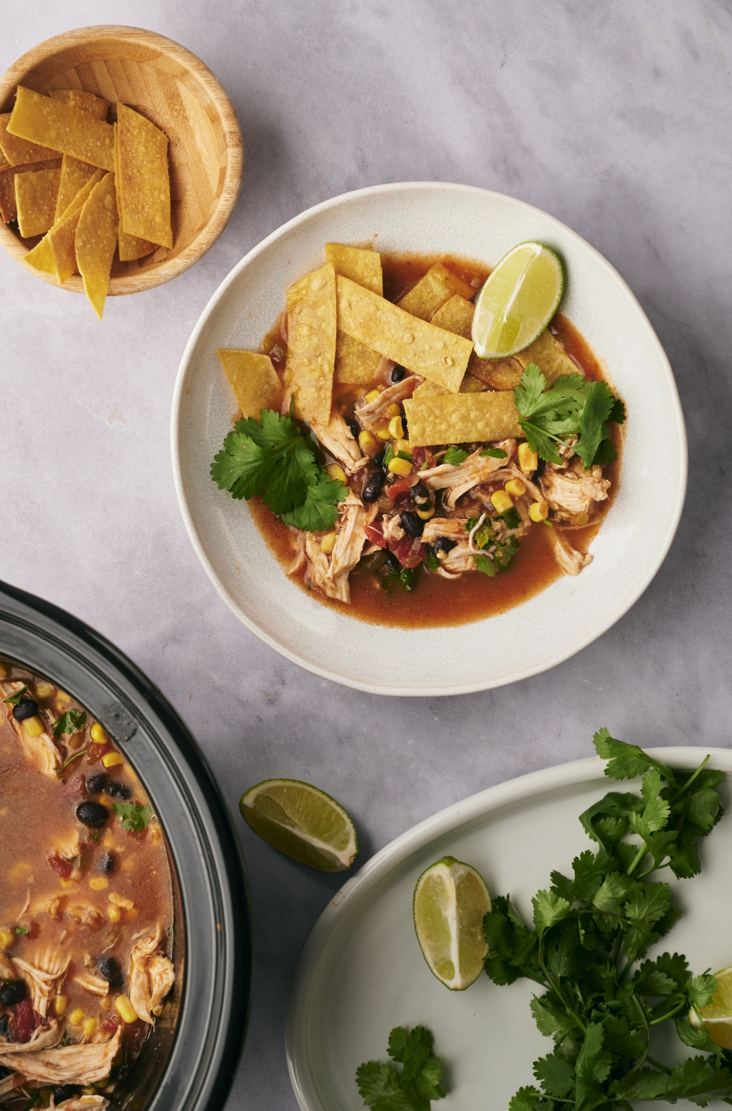 Slow cooker tortilla soup with shredded chicken, black beans, corn, and a spicy tomato broth served with crispy tortilla strips.