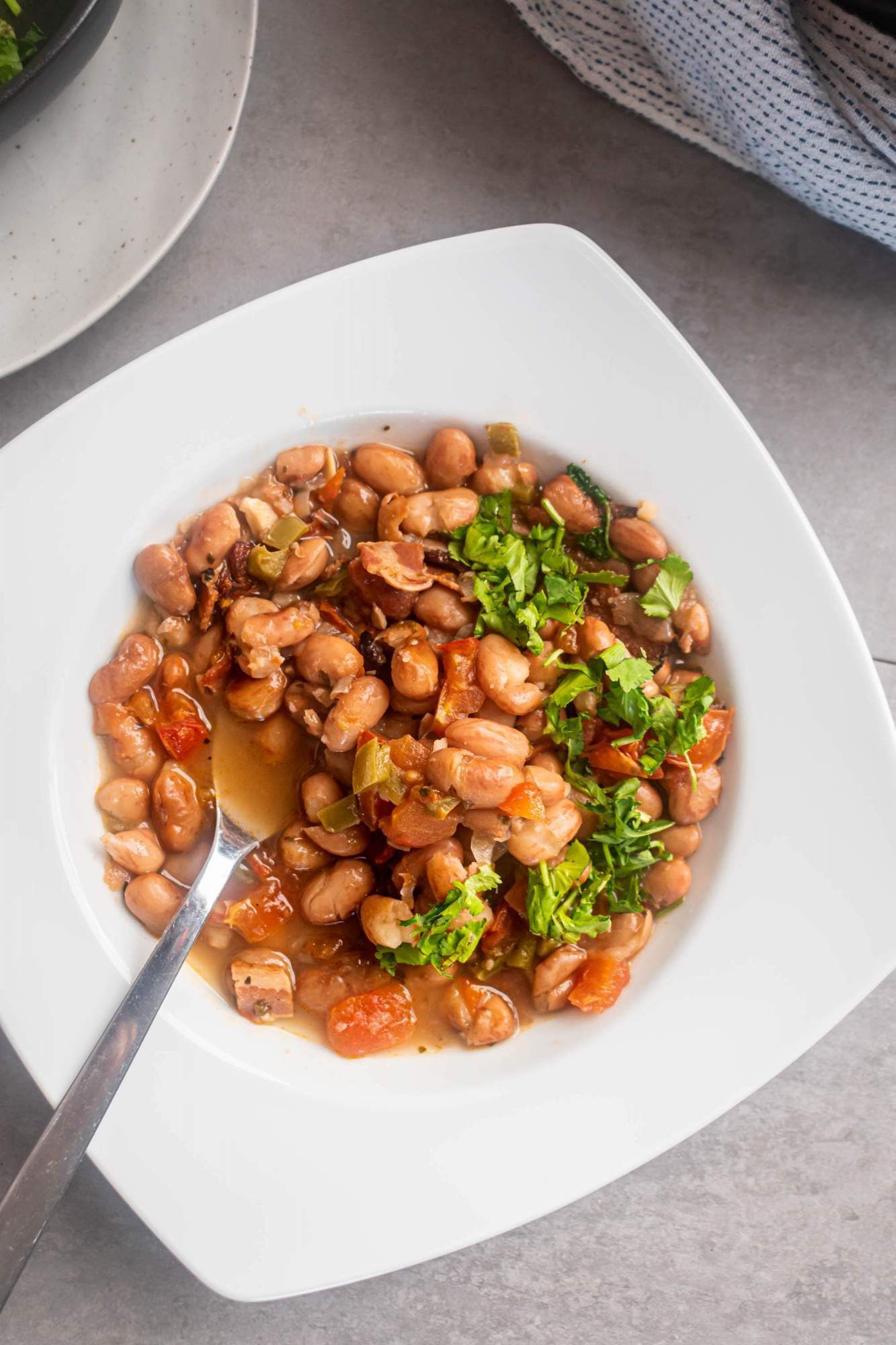 Mexican Charro beans with bacon, tomatoes, onions, garlic, spices, and jalapeños in a bowl with a spoon.