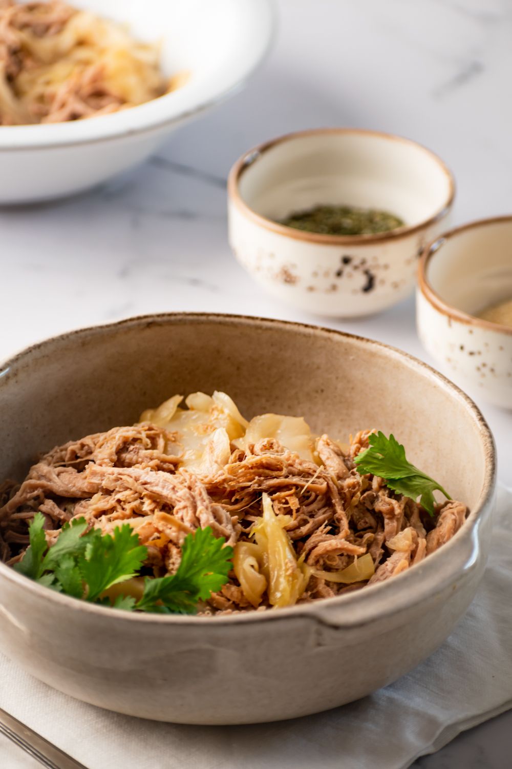 Kalua pork tenderloin shredded in a bowl with green cabbage and cilantro.