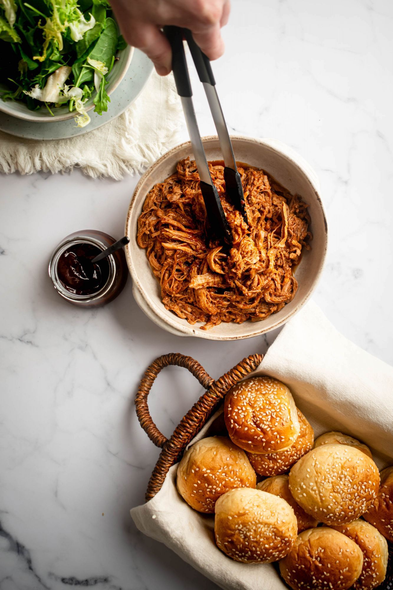 Crockpot pulled pork in a sweet and spicy barbecue sauce in a bowl with buns on the side.