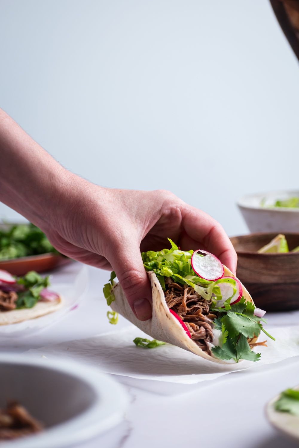 Shredded beef tri-tip tacos with lettuce and radishes being picked up. 