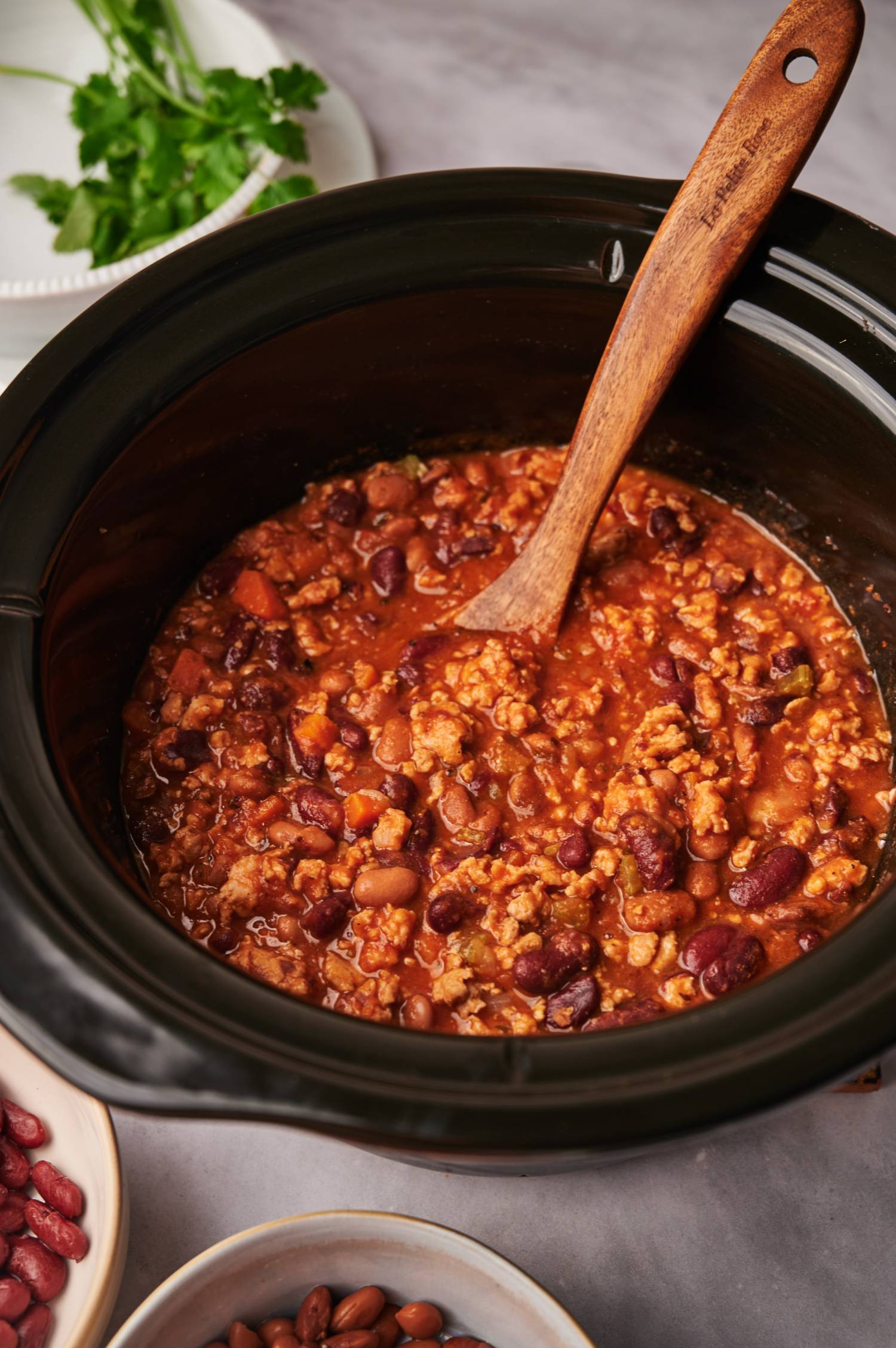 Ground turkey chili in a slow cooker with a wooden spoon and cilantro.