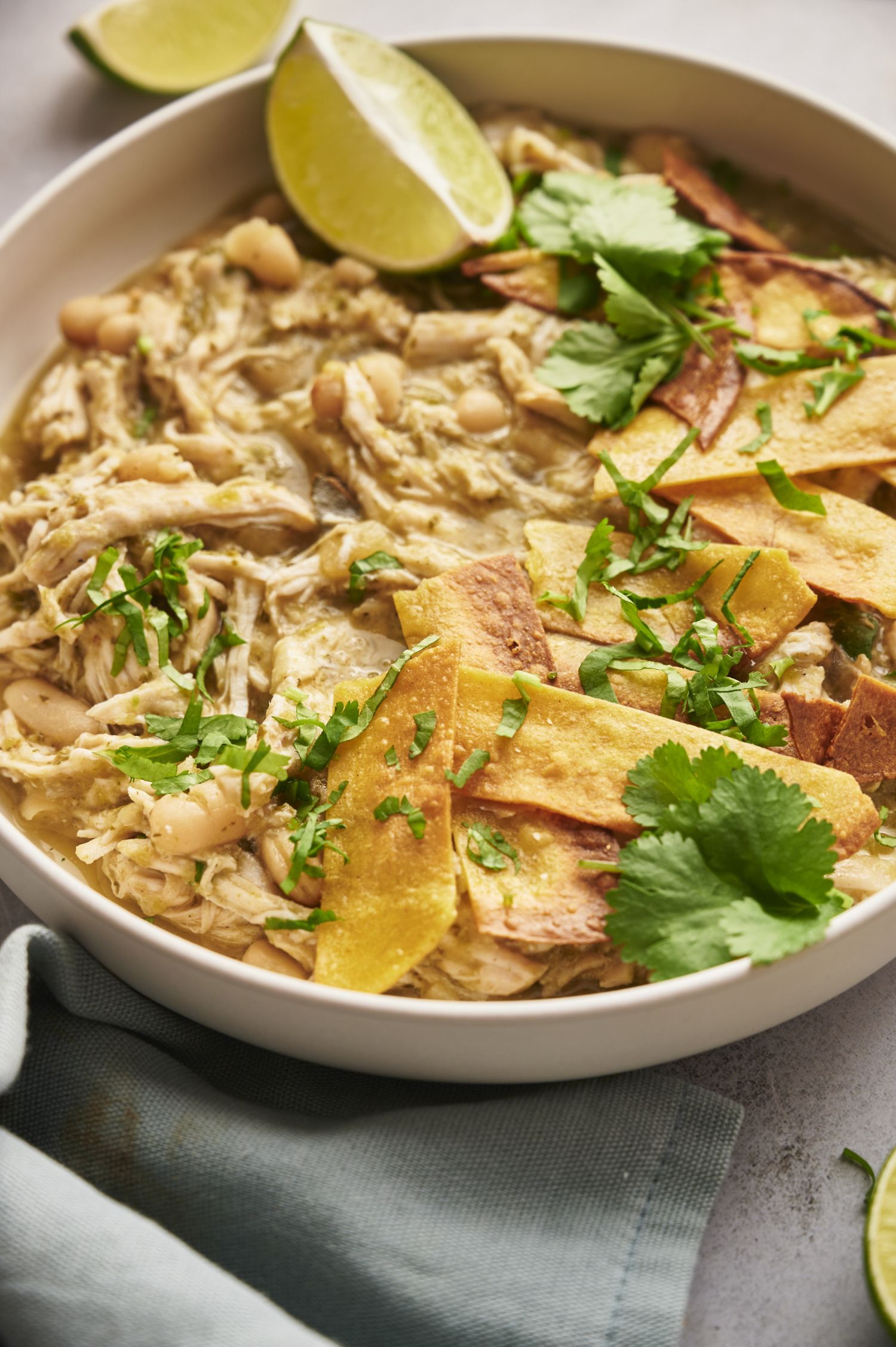 Chicken chili with white beans in a bowl with tortilla strips, cilantro, and lime.