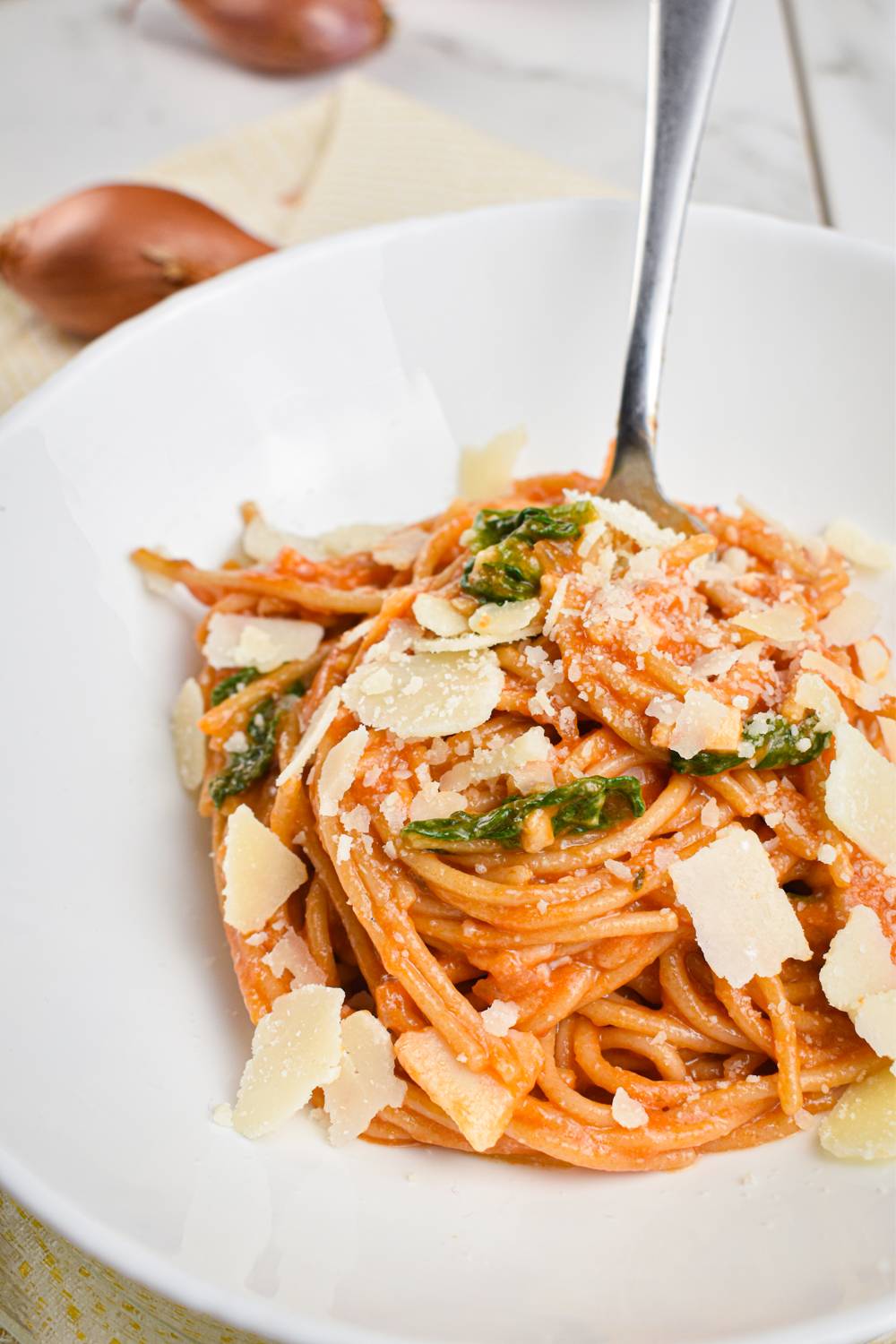 Spinach tomato pasta in a bowl with wilted spinach and Parmesan cheese.