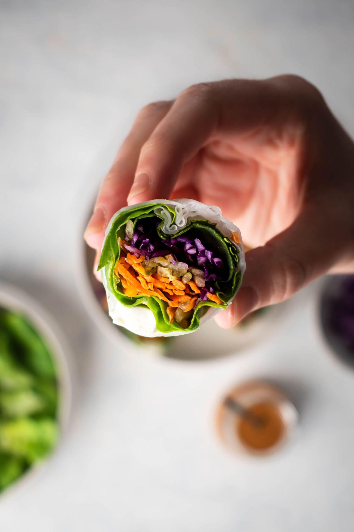 Hand holding a fresh spring roll filled with tofu and veggies.