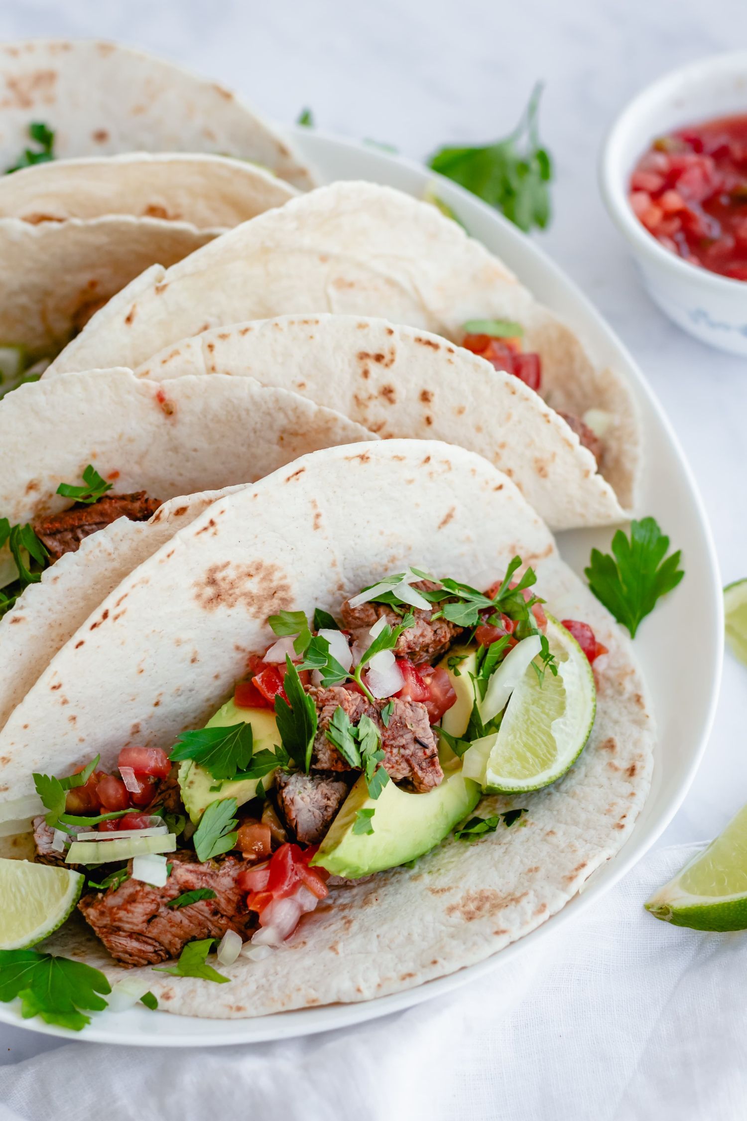 Grilled steak tacos with avocado and pico de gallo on flour tortillas.