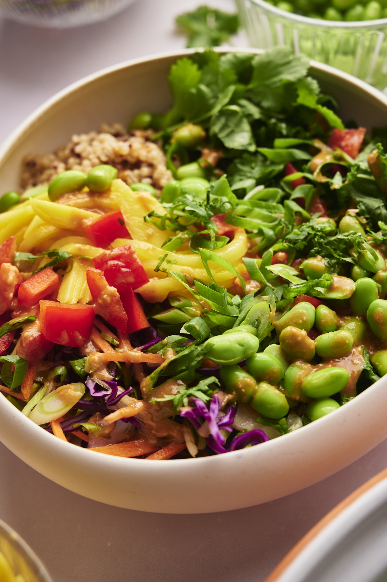 Thai inspired bowl with grains, fresh vegetables, peanut sauce, and herbs in a bowl.