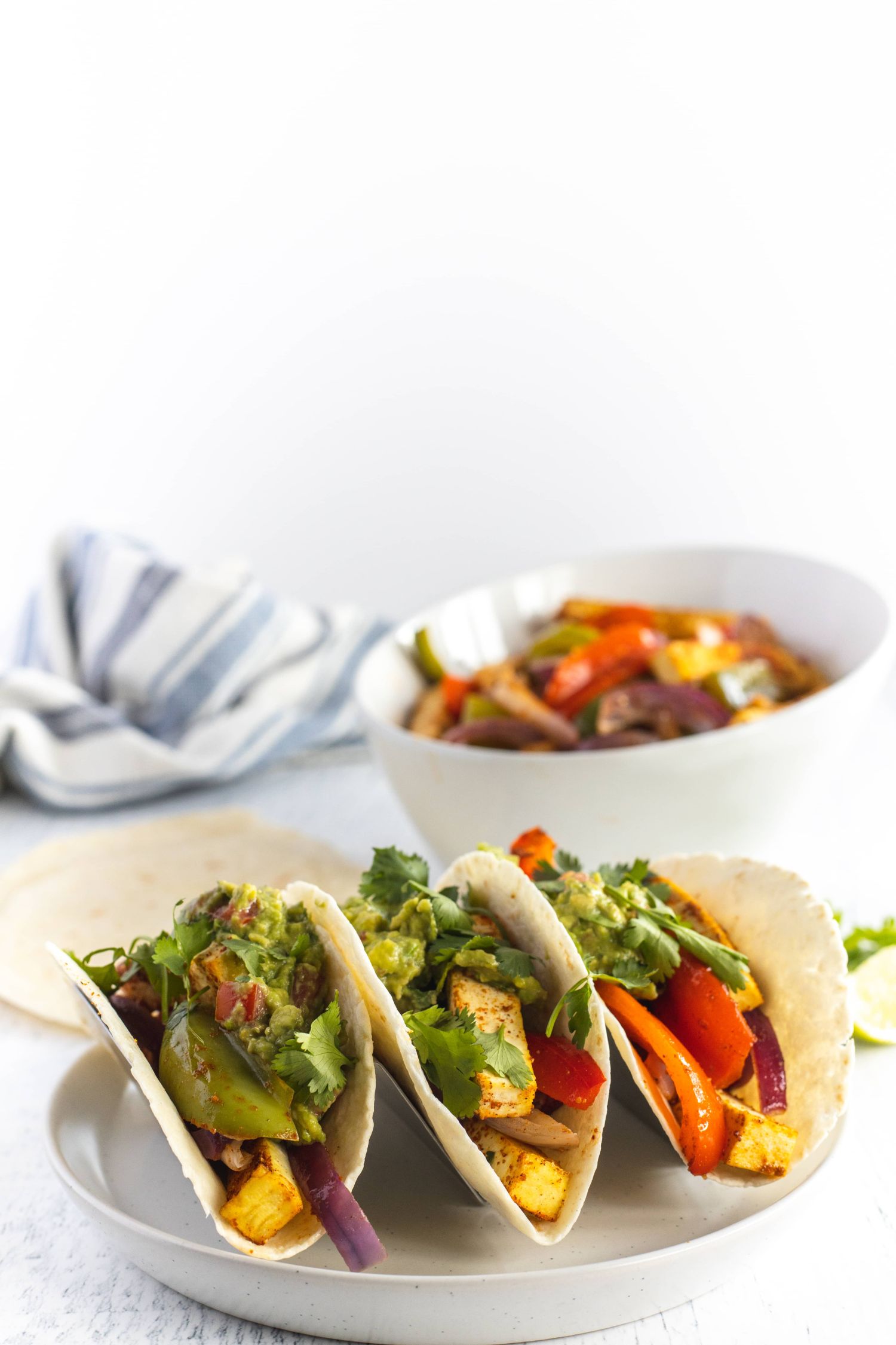 Oven baked tofu fajitas in flour tortillas with strips of tofu, peppers, onions, cilantro, and guacamole.