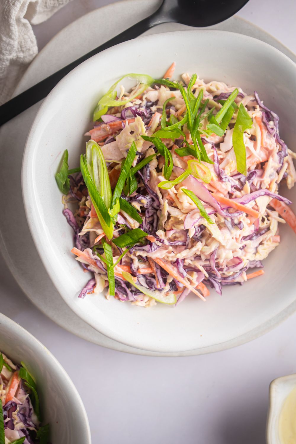 Bowl of coleslaw with a creamy yogurt dressing, green onions, and a black spoon.