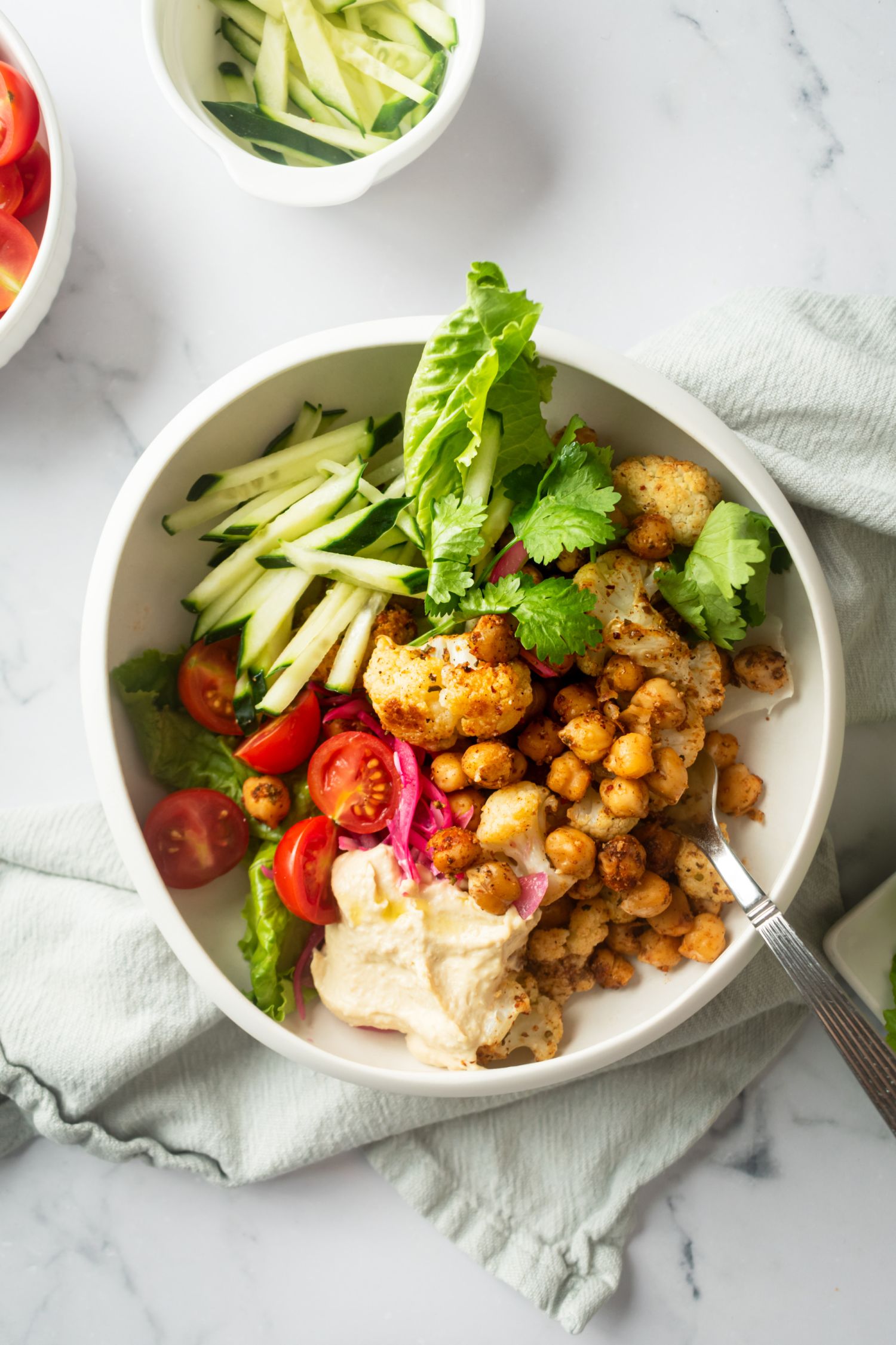 Roasted cauliflower and chickpeas with shawarma spices in a bowl with fresh veggies and herbs.