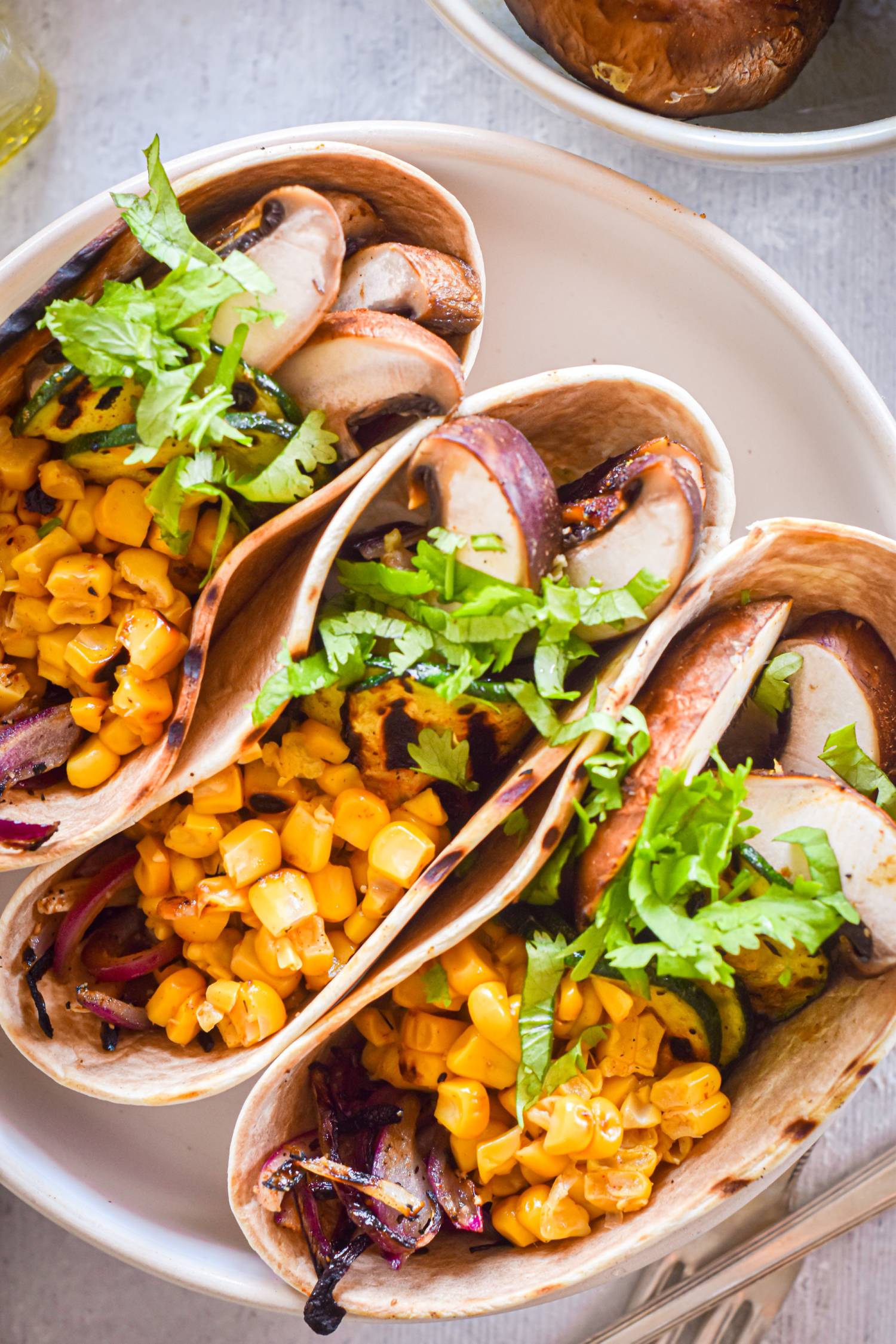 Corn, mushrooms, zucchini, and onion vegetable tacos served with cilantro and lime juice.