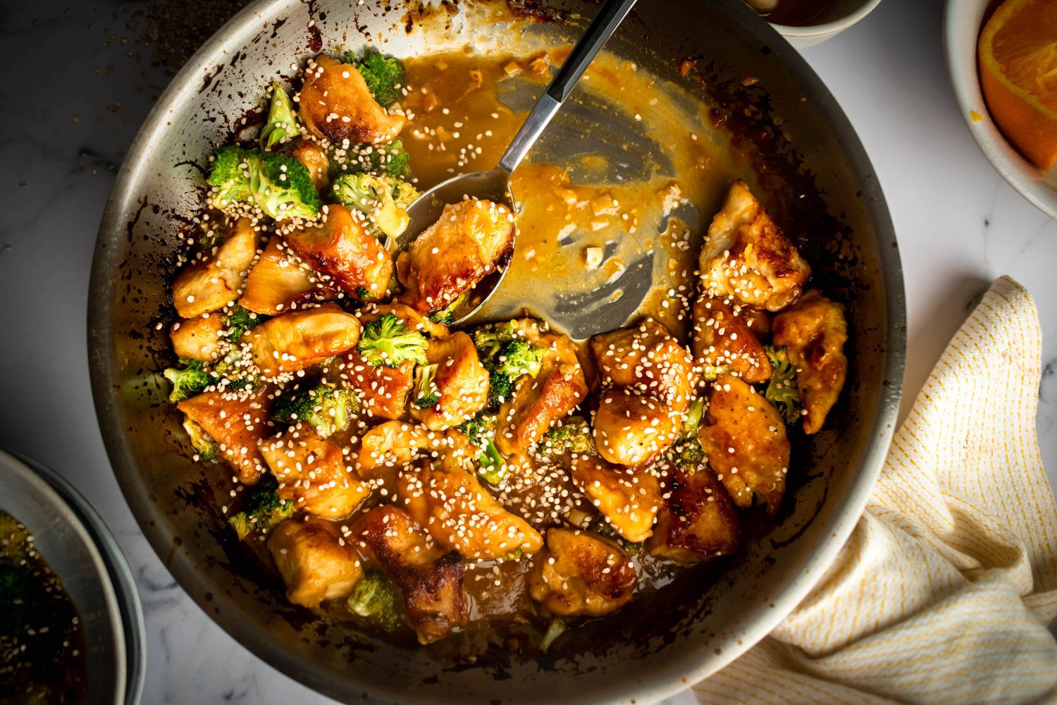 Stir fried orange chicken with broccoli in a heavy skillet with sesame seeds on top.