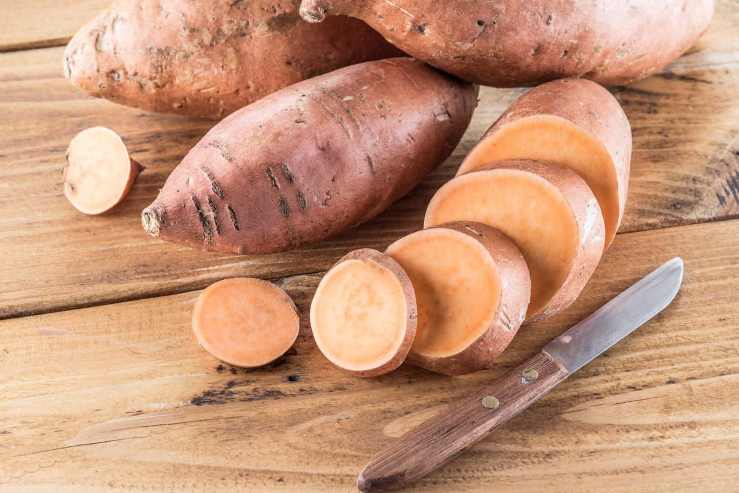 Sweet potato on a wooden cutting board with a knife.