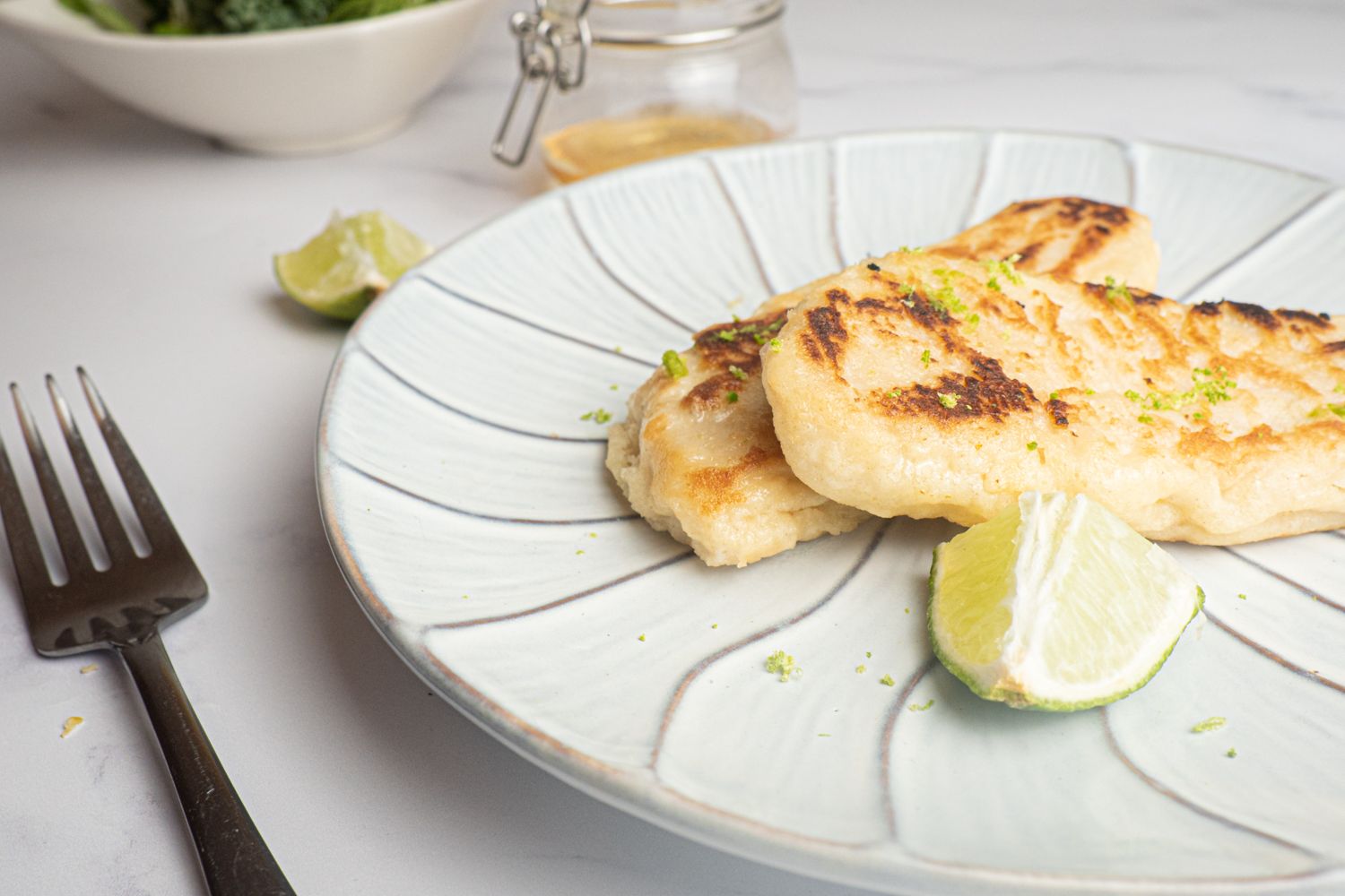 Tilapia with honey and lime cooked until crispy on a plate with a lime and fork.