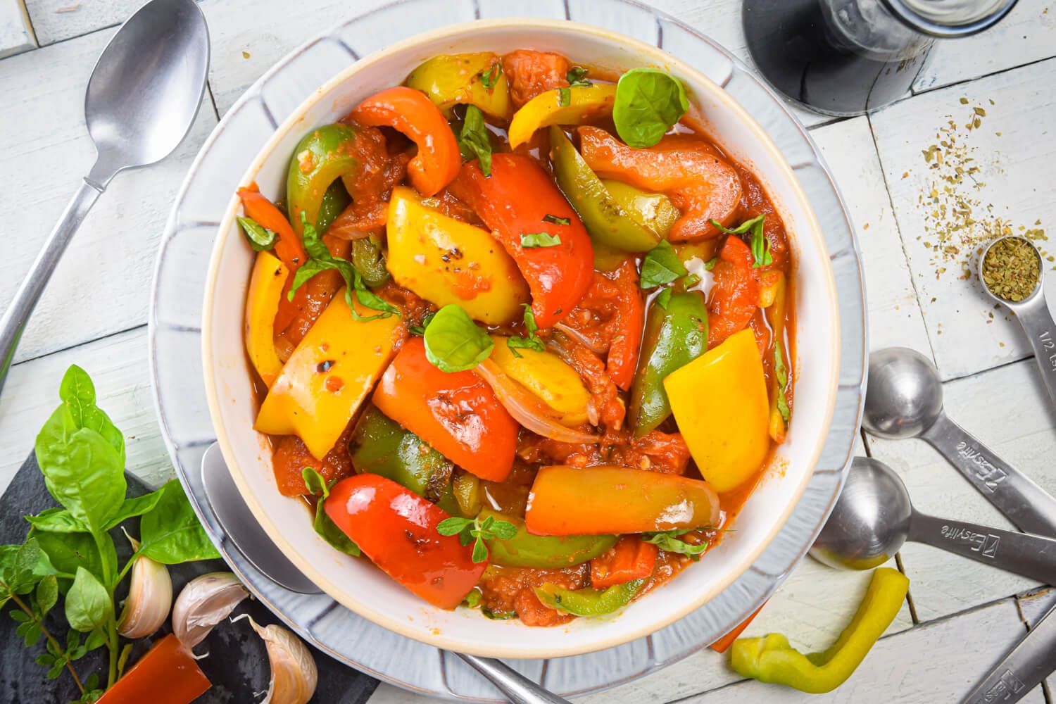 Pepperonata with bell peppers, sweet onion, Roma tomatoes, and garlic in a bowl with fresh basil and spices.