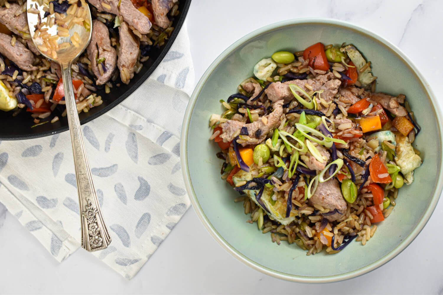 Pork fried rice with pork tenderloin, brown rice, carrots, peas, cabbage, and eggs in a bowl.