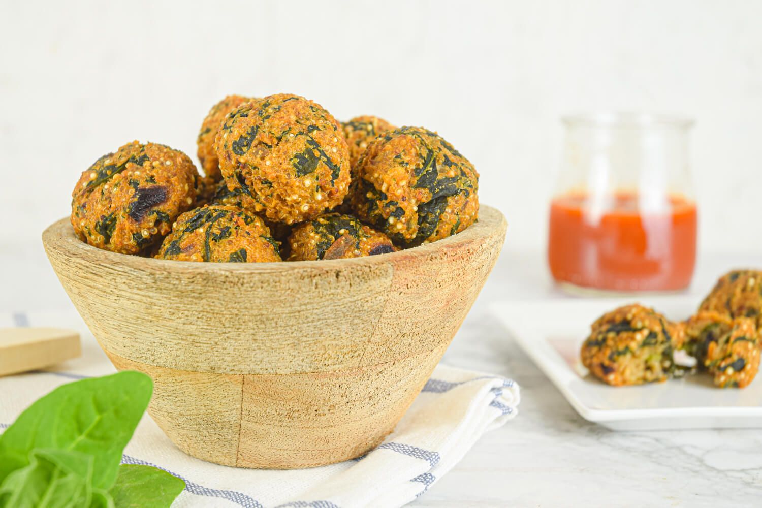 Quinoa meatballs with spinach in a bowl with basil and marinara sauce on the side.