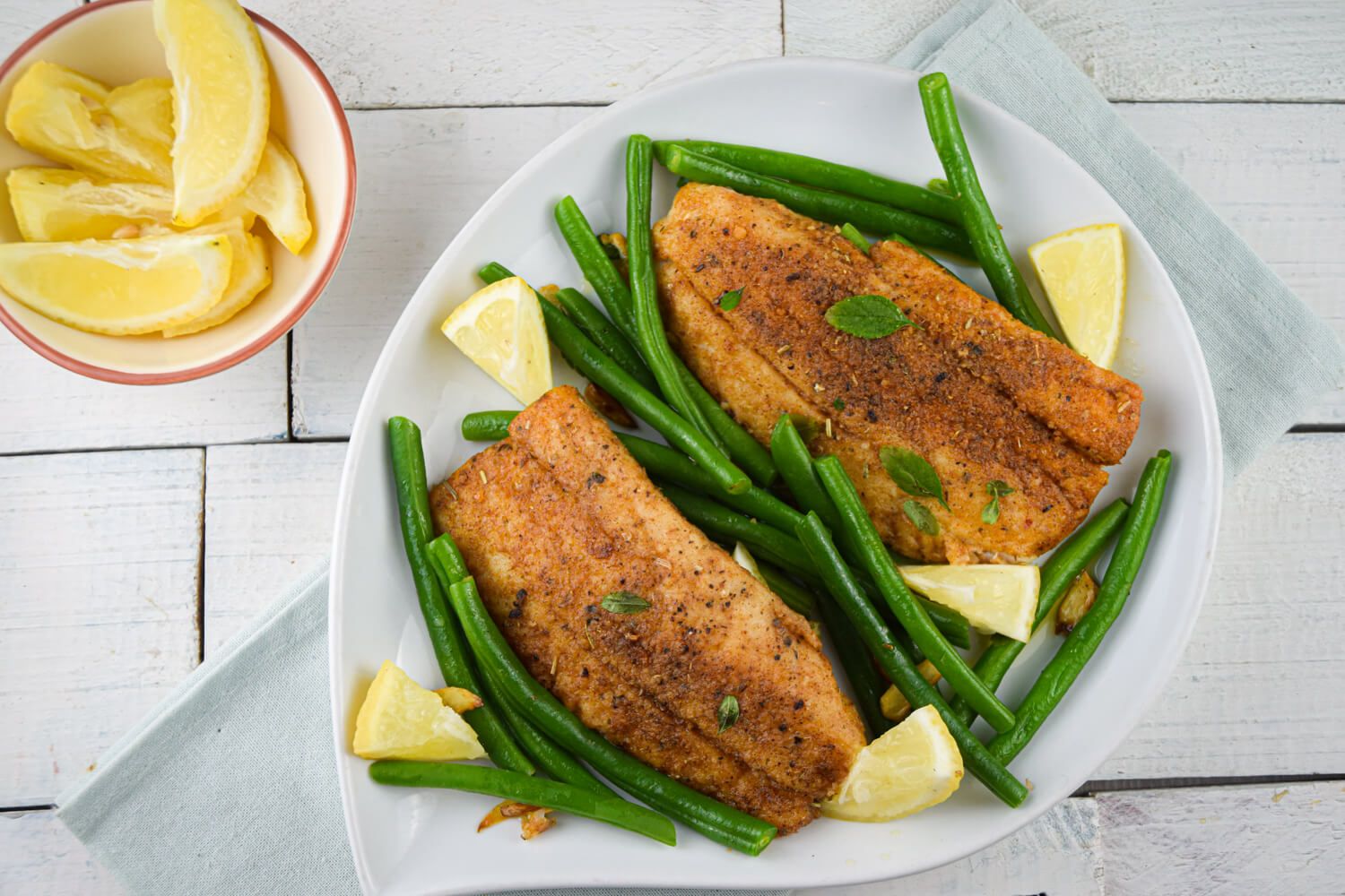 Tilapia with green beans, garlic, lemon, and a homemade spice rub on a plate. 